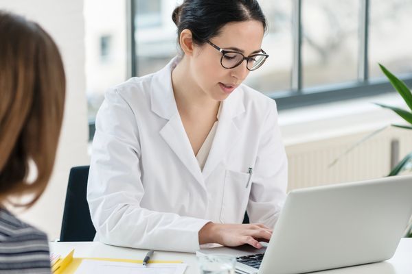 Lekarka pisze na laptopie podczas wizyty, pacjentka siedzi przed nią